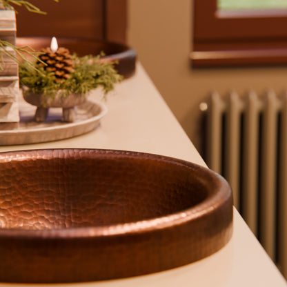 Round copper drop-in bathroom sink by Novatto with antique finish, traditional style, shown in a bathroom setting.