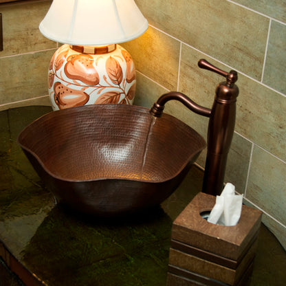 Traditional hammered copper bathroom vessel sink with scalloped edges in antique finish by Novatto, shown in a stylish bathroom setting.
