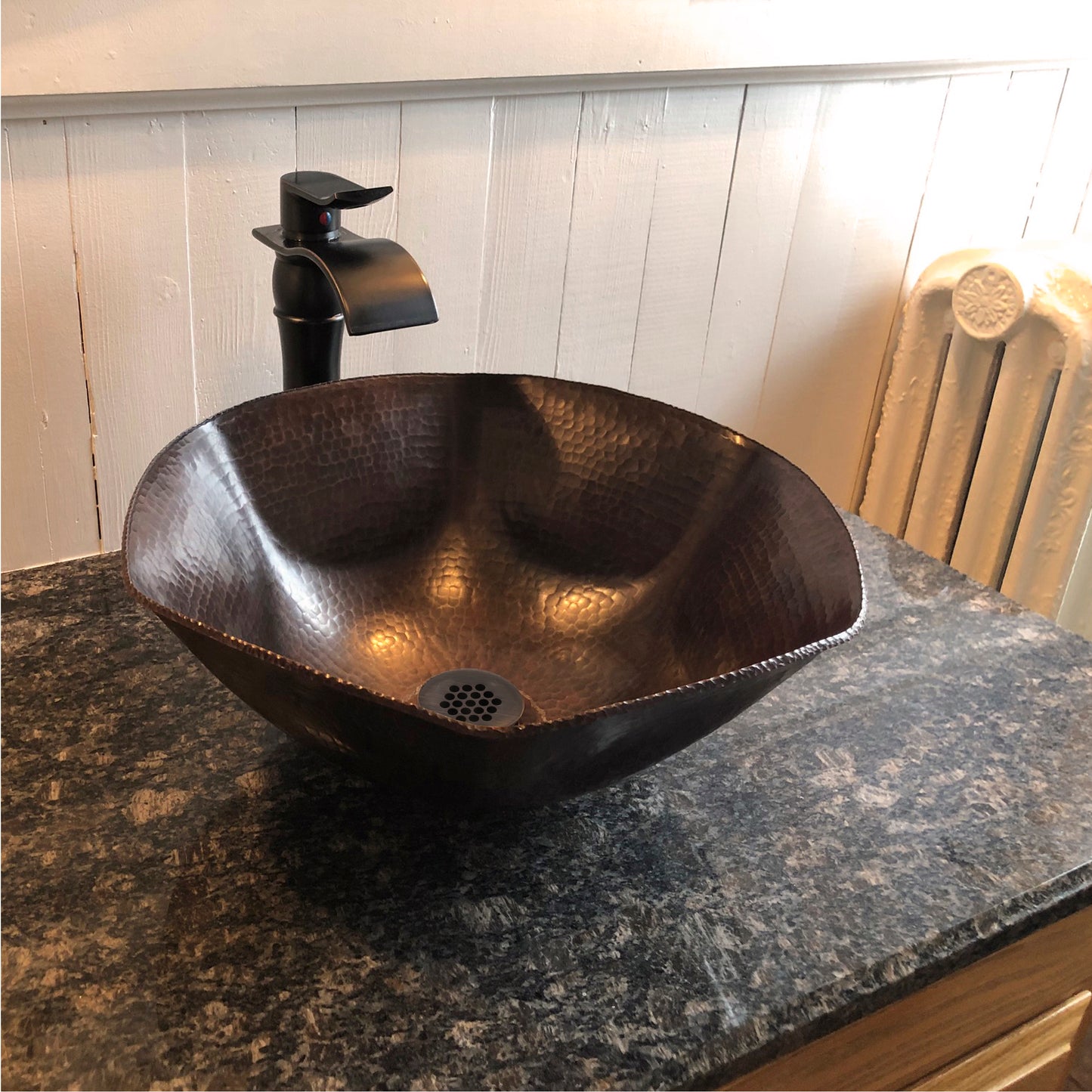 Traditional hammered copper vessel sink with scalloped edges in antique finish, styled for a bathroom setting by Novatto.