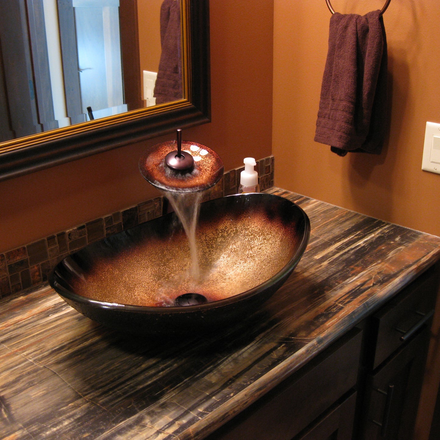 Black and copper oval glass vessel bathroom sink by Novatto, with a sleek transitional design and modern copper accents.