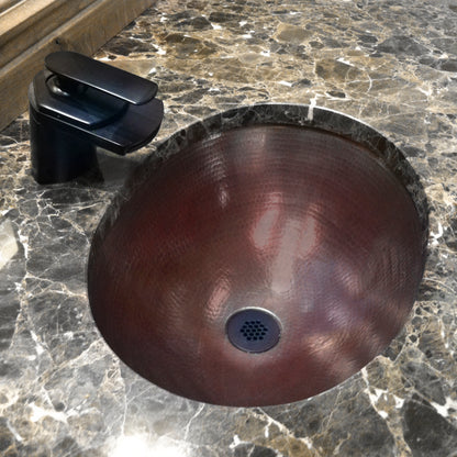 Traditional oval copper undermount bath sink by Novatto with antique finish, shown in a bathroom setting.