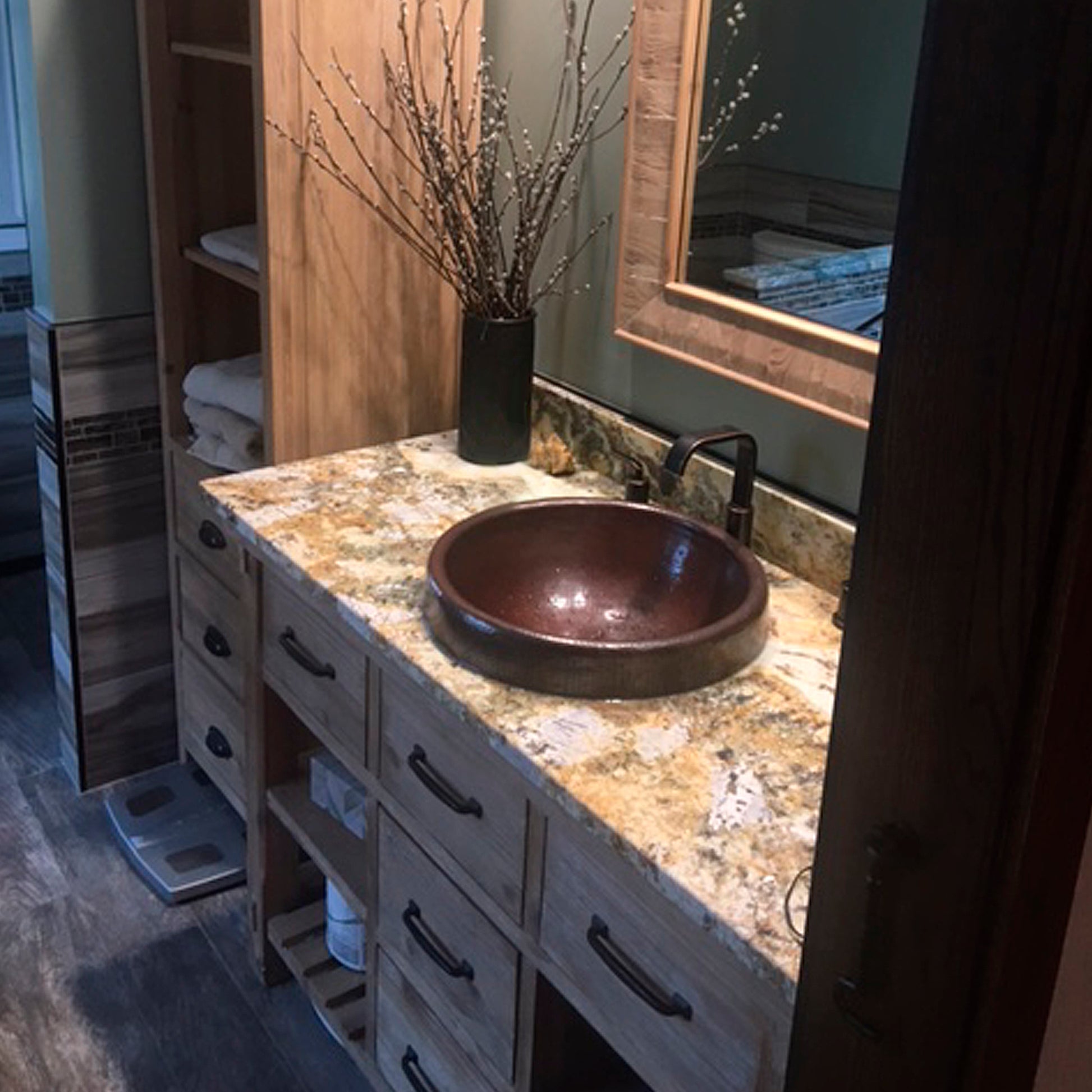 Round copper drop-in bathroom sink by Novatto with antique finish, traditional style, shown installed in a bathroom setting