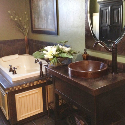 Round copper drop-in bathroom sink by Novatto with antique finish, traditional style, shown installed in a bathroom setting