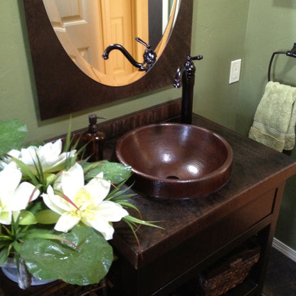 Round copper drop-in traditional bathroom sink by Novatto with antique finish, shown installed in a bathroom setting.