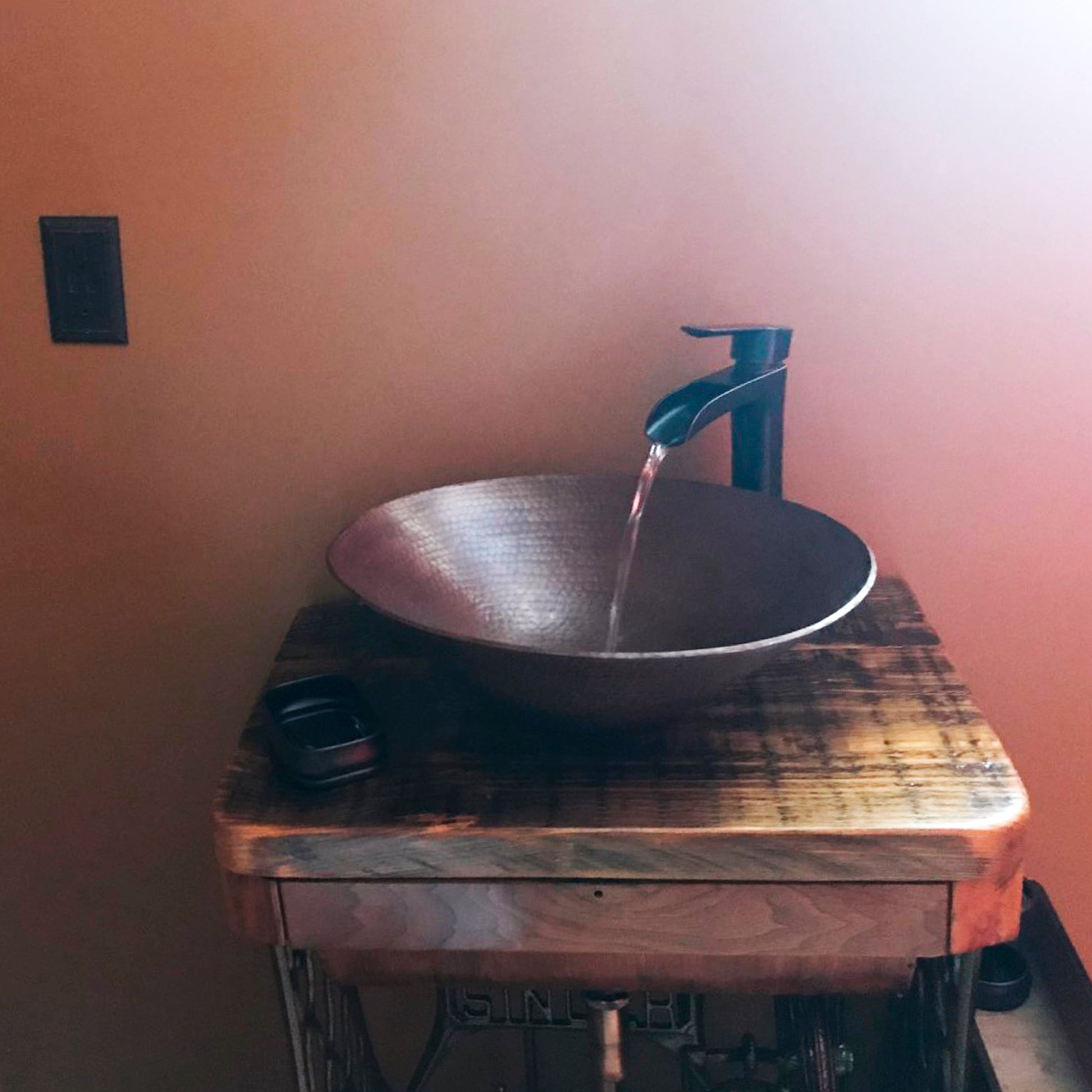 Traditional oval hammered copper vessel bathroom sink with antique finish by Novatto, shown in a stylish bathroom setting