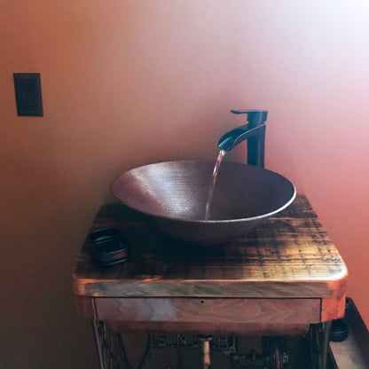 Traditional oval hammered copper vessel bathroom sink with antique finish by Novatto, shown in a stylish bathroom setting